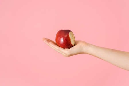 A bitten red apple in an open female palm on a pink backgroundの写真素材