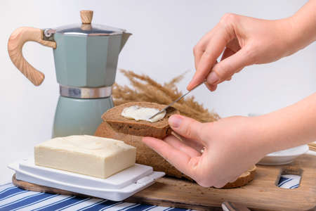 A woman's hand makes a sandwich with butter and rye bread