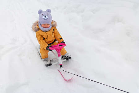 Toddler 12-23 months old sitting on a children's snowcat is pulled by a rope, front viewの写真素材