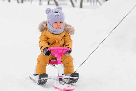 Toddler aged 12-23 months rides a snowcat holding the steering wheel in a winter park during a snowfallの写真素材