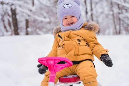 Portrait of a joyful toddler 12-23 months old sitting on a children's snowcat in a winter park. Active lifestyle in winterの写真素材