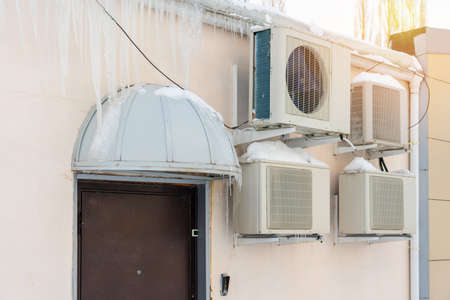 A lot of air conditioning units on the outer wall of an office building. Icicles hanging from the roof of the building. Winter time.の写真素材