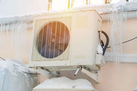 A broken air conditioner unit on the outside wall of an office building. Icicles hanging from the roof of the building. close-up.の写真素材