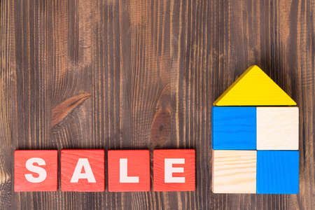 The concept of selling real estate. Words SALE on red wooden cubes, a house made of wooden blocks on a brown background.の写真素材