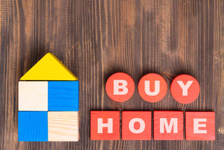 The concept of buying real estate. The phrase BUY HOME on red wooden cubes, a house made of wooden blocks on a brown background.の写真素材