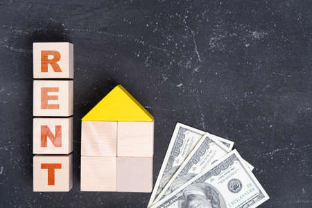 The concept of renting real estate. The word RENT on toy cubes, a house made of wooden blocks and dollar bills on a dark background, top viewの写真素材