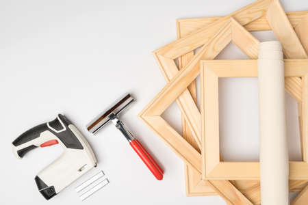 A stack of wooden stretchers for the canvas and a tool for stretching it. Pliers and battery gun for staples on a white background, copy spaceの写真素材
