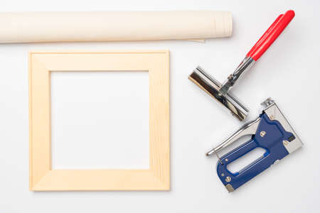 Tools for stretching a canvas with a photo on a wooden stretcher. Square stretcher, canvas roll, tongs and a gun for staples on a white background, top viewの写真素材