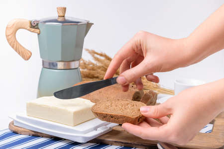 Cooking breakfast, a woman's hand with a piece of rye bread applies butter with a table knife.の写真素材