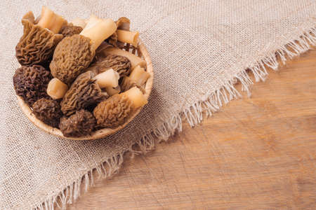 A wicker basket with morel mushrooms stands on a burlap cloth lying on a brown wooden backgroundの写真素材