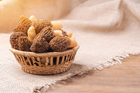 Morel mushrooms collected in the forest in a wicker basket on a wooden background are covered with...