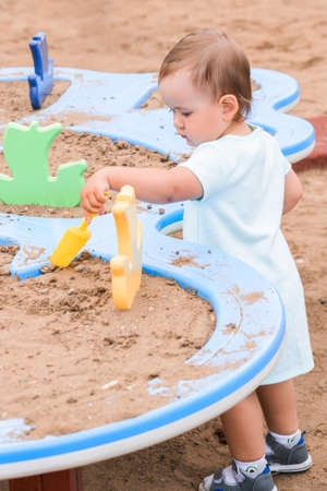 a girl 2-3 years old plays in the sandbox plays in the sandbox with a shovelの写真素材