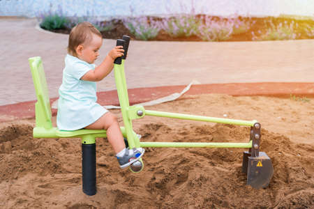 A 2-3-year-old girl drives a toy excavator on a playgroundの写真素材