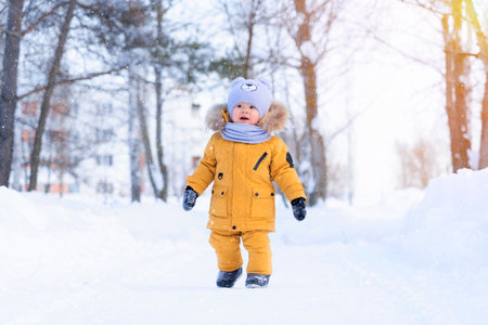 A baby sees snow for the first time. Portrait of a toddler 15-20 months old in yellow warm clothes in a winter park happily looking at snowflakesの写真素材