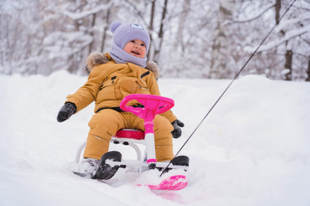 An active lifestyle in winter. A happy toddler sits on a children's snowcat and enjoys driving fast in the snowの写真素材