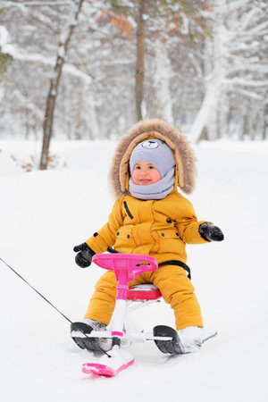A happy child 12-23 months old laughs while riding a children's snowcat in a winter parkの写真素材