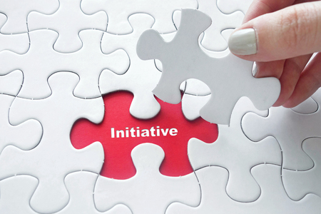 Close up of girl's hand placing the last jigsaw puzzle piece with word Initiative as business conceptの写真素材