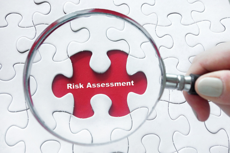 Word Risk Assessment with hand holding magnifying glass over jigsaw puzzleの写真素材
