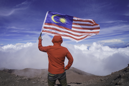 A man holding national flag of Malaysia near mountain cliffの写真素材