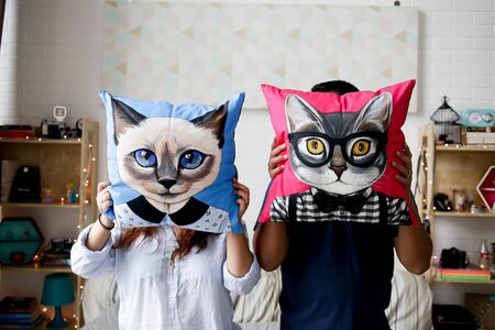 a couple holding a pillow with cat cover to hide their faceの写真素材