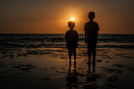 A shot of two boys standing in front of the ocean enjoying the sunsetの写真素材