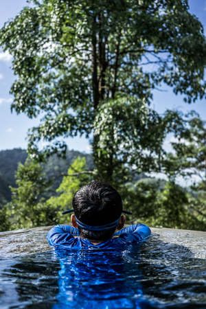 A shot of a boy at the corner of an infinity pool enjoying the nature in front of him.の写真素材