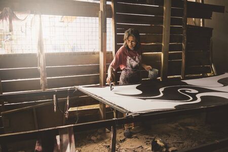 Kota Bahru, Kelantan Malaysia, 15th July, 2017 - A shot of a local Kelantanese woman coloring the batik outlined by wax. The shot was taken at one of the villages in Kelantan that practices the traditional ways of producing batik fabrics.のeditorial素材