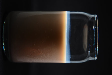 Clear view of fresh full cream milk in a glass with visible condensation droplets against a solid...