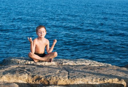 young smiling boy meditating at sea coastの写真素材