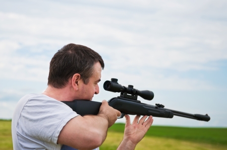 man aiming, looking into the scope of his rifle