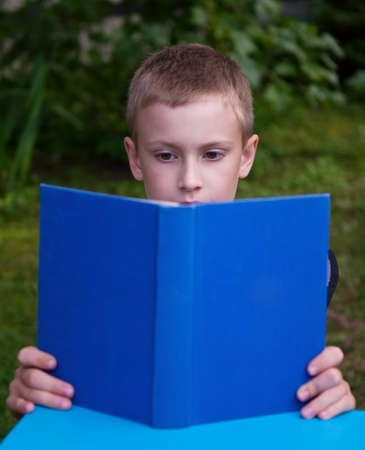 8-year schoolboy reading blue book outdoorsの写真素材