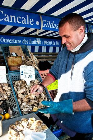 Cancale, Brittany, France - November 1, 2012: Oysterman opening oysters at oyster market of Cancale, France.のeditorial素材