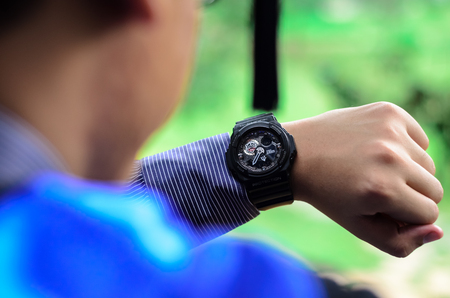 A male university graduate is looking at the time on his wrist watch. Soft focus, shallow DOF with bokeh background.のeditorial素材