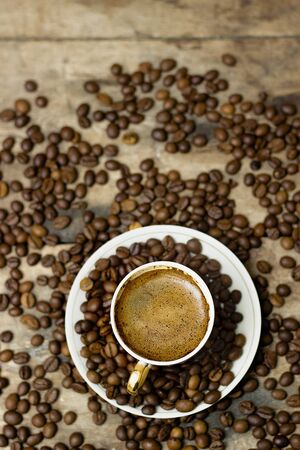 A cup of cappuccino with scattered coffee beans in a brown wooden tableのeditorial素材