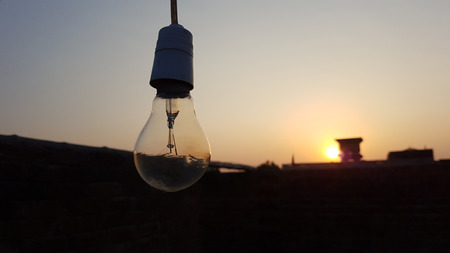 Light bulb with sunset and black buildings background