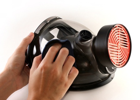 Hands cleaning a black gas mask with a piece of blue clothの写真素材