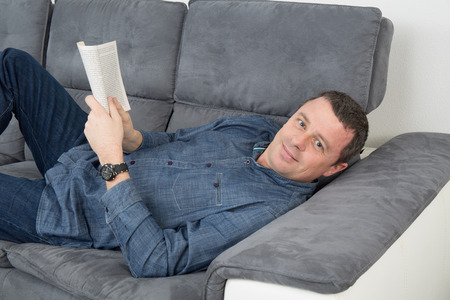 Smiling handsome mature man relaxing enjoying a book on the sofaの写真素材