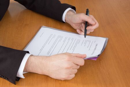 Businessman in dark suit and blue shirt sitting at office desk signing a contract with shallow focus...
