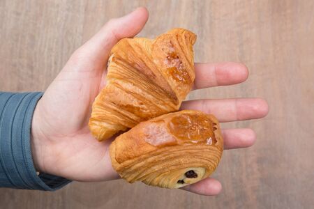 Hand holding a  fresh croissant and chocolatine on wooden backgroundの写真素材