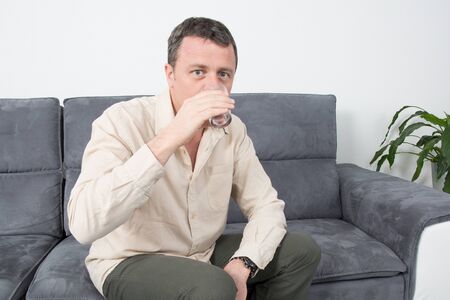 Picture of a happy man sitting on couch in house drinkingの写真素材