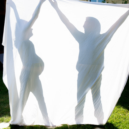 Shadows of a couple behind a sheet -Symbol of a pregnancyの写真素材