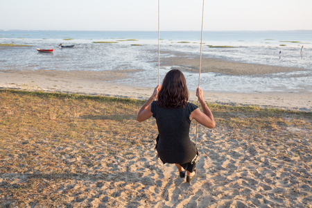 Back view of a woman  on a swing on a beach  watching oceanの写真素材