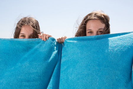 Two girls have fun at the beach with towelの写真素材
