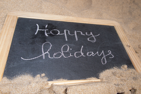 Happy holidays written in a board on sand, on tropicalの写真素材