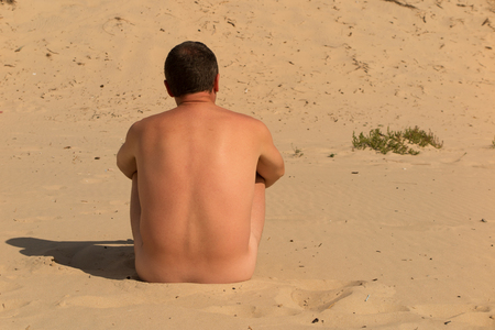 Portrait  of a naked man sitting alone on the beachの写真素材