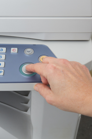 Woman holding finger on start button of laser printerの写真素材