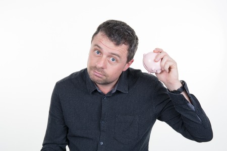 Happy young man putting money in piggy bank isolated on white backgroundの写真素材
