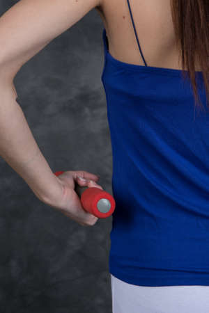 Rear view of young female with dumbbells doing exercises in gymの写真素材