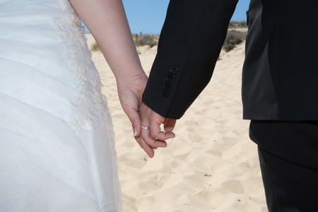 Couple on the beach in wedding dress holding handsの写真素材