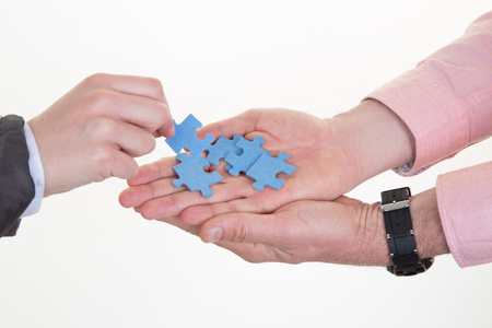 Woman taking puzzle pieces in hand of man in officeの写真素材